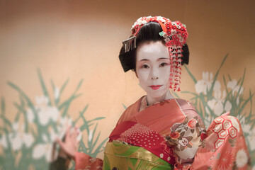 Japanese Maiko or geisha in red kimono against a wall with a pattern of tradional iris flowers.