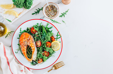 Grilled Salmon steak and fresh vegetable salad with a lemon over white marble background. Healty food concept