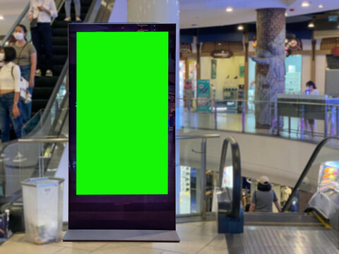 Shot of a Floor-Standing LCD Touch Screen Display with Green Screen Chroma Key Mock Up Standing in Shopping Mall. Busy shoppers buying retail products. Consumerism and retail topics