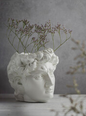 Close-up of a white plaster statue of the head of David on a gray concrete background. Minimalist artistic flower poster. Ancient Greek sculpture. - obrazy, fototapety, plakaty