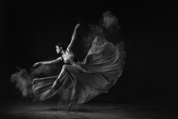 Grayscale shot of an emotional Southeast Asian ballet dancer performing a move on a black background - obrazy, fototapety, plakaty