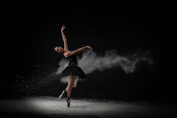 Emotional Southeast Asian ballet dancer in a black dress performing a move on a black background - obrazy, fototapety, plakaty