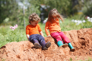 Little brother and sister play on a pile of sand on a clear day.