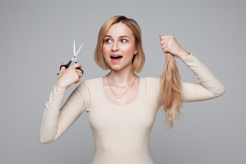 Studio portrait of blonde female cutting her own hair, hairstyle and haircut, lock of hair,...
