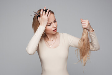 Studio portrait of blonde female cutting her own hair, hairstyle and haircut, lock of hair,...