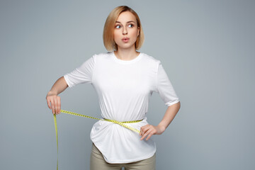 Close up blonde woman in white shirt measuring her waist with yellow measuring tape. Weight loss,...