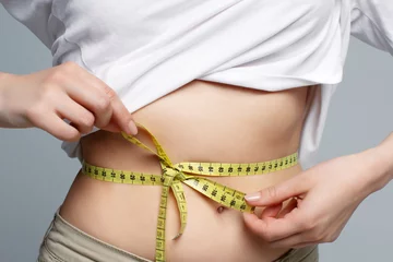 Foto op Plexiglas Close up woman in white shirt measuring her waist with yellow measuring tape in bow. Weight loss, slim body, healthy lifestyle concept. Figure control and counting calories. Successful diet plan. © Eva March