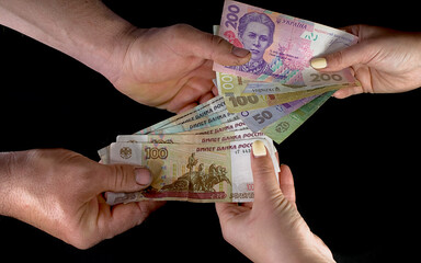 Russian rubles and Ukrainian hryvnia in the hands of a man exchange. On a black background