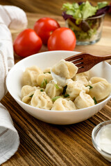 dumplings with sour cream, herbs on a wooden table. vegetables and table napkin at the back