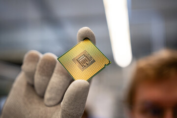 A CPU with clean, golden contacts held in the hand with some ESD gloves
