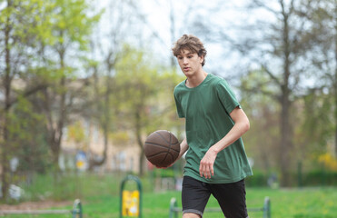 Cute young teenager in green t shirt with a ball plays basketball on court. Sports, hobby, active lifestyle for boys