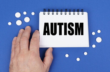 On the blue surface of the tablet, a hand and a notepad with the inscription - AUTISM