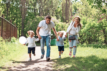 Family of four running on path outdoors at park at sunny day. Father, mother and two boys twins holding hands walking at countryside. Outdoor weekend activity, celebrating holidays, maternity goals