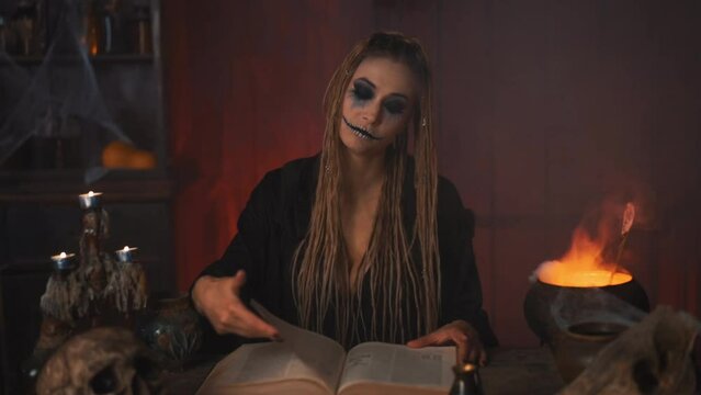 Halloween, witch reading magic book use cauldron prepare poison or love potion. Black magic occult female wizard sitting on the table dark room spider web human skull Necromancer. voodoo. Handheld