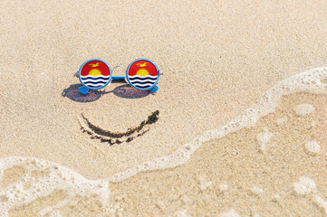 Fototapeta na wymiar A painted smile on the sand and sunglasses with the flag of the Kiribati. The concept of a positive and successful holiday in the resort of the Kiribati.