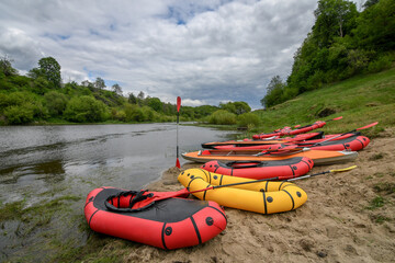 Packraft rubber boats and kayaks on sandy river bank, with dramatic sky. Selective focus. Active lifestyle concept.