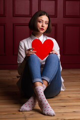 Short-haired woman sitting on floor legs crossed holding heart shape on her knees