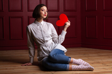 Short-haired woman sitting on floor holding heart shape like a hand fan