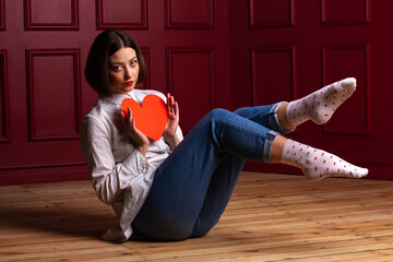 Short-haired woman sitting on floor legs in air holding heart shape in front of her chest