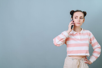 A girl on a soft blue background with a funny hairstyle is talking on the phone in disbelief