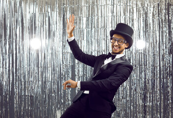 Funny cheerful young guy having fun at party. Happy black man in suit, glasses, bow tie and classic...