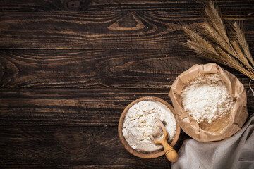 Obraz na płótnie Canvas Wheat flour in a bowl on a wooden rustic background with spikelets.