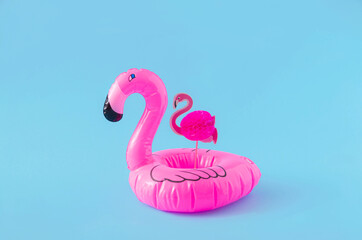 A small pink flamingo in a bigger plastic flamingo against blue background. Minimal creative...