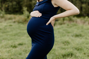 Young 38 weeks pregnant woman in a blue dress holding her belly