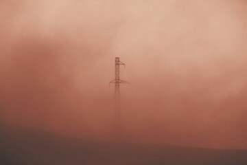 Electric power transmission lines in smoke. High voltage post. Industrial landscape. Electricity pylon at sunset sky on the background. Electric distribution station