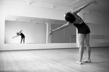 Black and white photo of young woman performing emotional dance in front of mirror in dancing hall,...