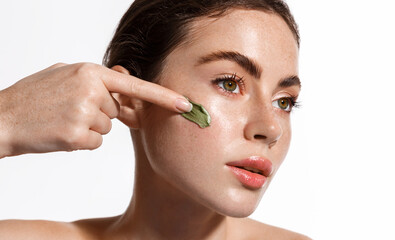Skin care. Woman looks in mirror, applies facial clay mask, cleansing scrub, face cream from...