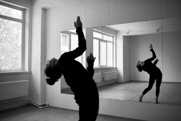Black and white photo of female dancer rehearsing in front of mirror in dancing hall