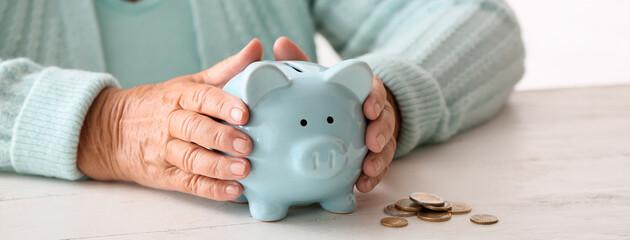 Senior woman with piggy bank sitting at table. Concept of pension - obrazy, fototapety, plakaty