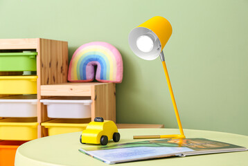 Modern lamp, toy car and book on color table in children's room