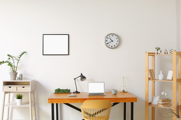 Modern laptop, cup and mobile phone on wooden standing desk near light wall