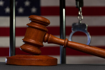 The judge's wooden hammer on the background of bars, handcuffs, the American flag. Concept: court...