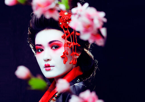 young pretty real geisha in kimono with sakura and decoration on black background