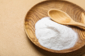Plate with baking soda and spoon on beige background, closeup
