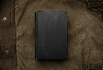 A closed book with a black cover on an old hiking backpack. Vintage khaki canvas back.