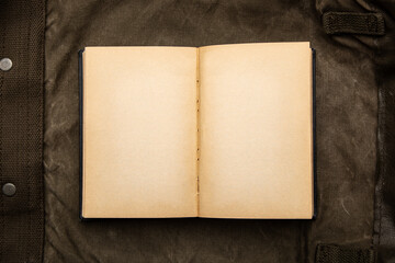 An open book with yellowed pages on an old backpack. Vintage khaki canvas back.
