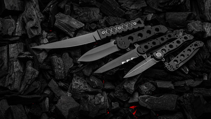 Modern knives with black blades. Hunting, military and folding knives on smoldering charcoal. Black...