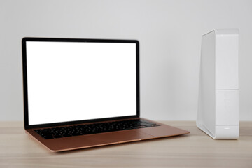 Modern laptop and wi-fi router on table near white wall