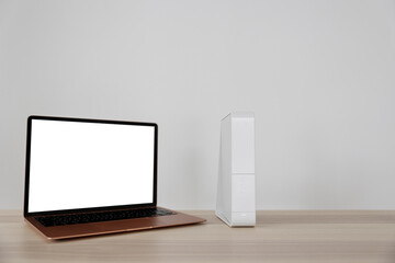 Modern laptop and wi-fi router on table near white wall
