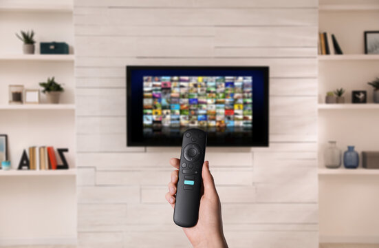 Woman with remote control changing channels while watching TV at home, closeup