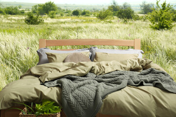 Comfortable bed with soft pillows in meadow on sunny day