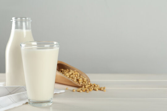 Fresh soy milk and grains on white wooden table. Space for text