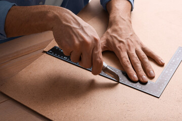 Man cutting chip board with utility knife and ruler at table, closeup