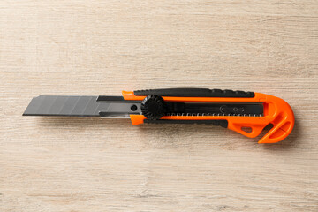 Orange utility knife on white wooden table, top view. Construction tool