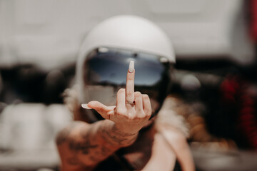 Cool rebellious motorcyclist girl in a helmet with tattoos showing middle finger