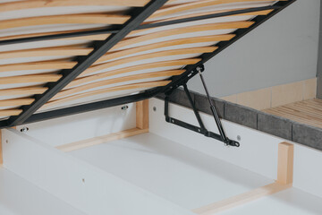 Closeup shot of a bed with wooden frame and lifting mechanism for a storage space
